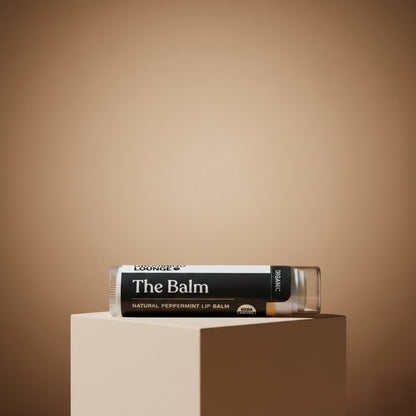 Lip balm labeled 'The Balm' on a beige pedestal against a brown background